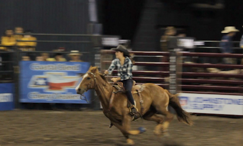 Showing a woman riding a horse during a barrel racing event.